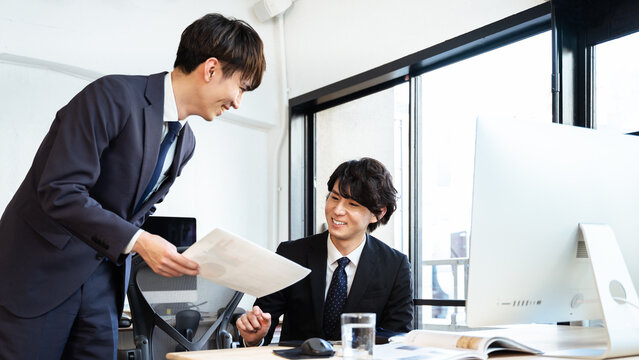 インターンシップの若者に和やかに仕事を教える広告代理店の職場にいるビジネスマンの男性