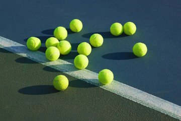 Come on, toss one. Shot of an empty tennis court and tennis balls during the day.