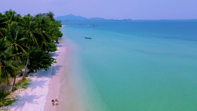 A couple of men and women on vacation at Koh Mook tropical Island in the Andaman Sea in Thailand, men and women walking on a beach with palm trees drone aerial view at the beach of Koh Mook