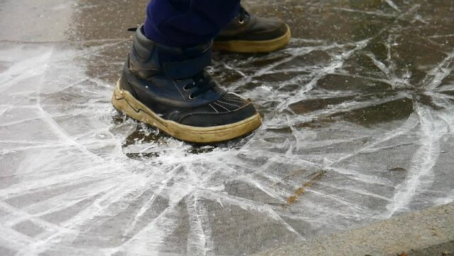 Close-up of the shoes of a boy jumping on an icy puddle and breaking the ice