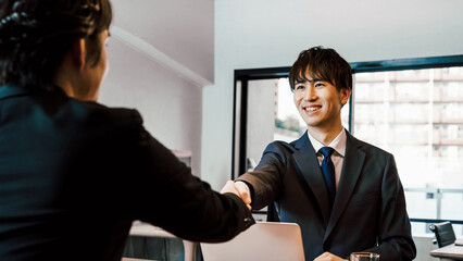 オフィスの会議室で笑顔で握手をする中小企業やスタートアップのビジネスマンの男性2人
