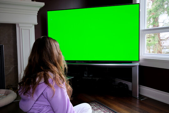 Watching Tv Green Screen Dolly Shot. Ponytail girl watching big screen television at home, dolly shot. Green screen footage. point at the TV screen High quality