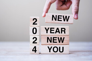hand holding wooden block with text 2024 NEW YEAR NEW YOU on table background. Resolution, strategy, goal, business and holiday concepts