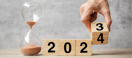 hand flipping block 2023 to 2024 text with hourglass on table. Resolution, time, plan, goal,...