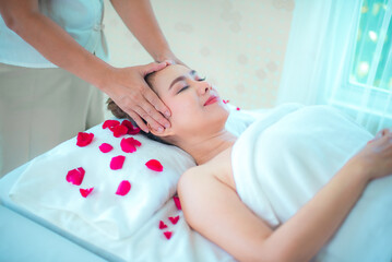 Obraz na płótnie Canvas Professional masseuse head massage to asian woman on bed sprinkled with rose petals.