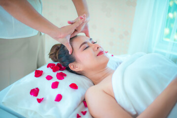 Obraz na płótnie Canvas Professional masseuse head massage to beautiful asian woman on bed sprinkled with rose petals.