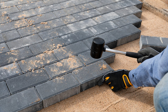 Laying cement pavement on a walkway with a rubber hammer and gloves on a sand. House improvement.