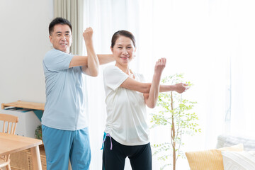 家で運動するシニア夫婦（肩のストレッチ） © polkadot