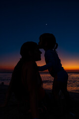 hija dandole beso tierno a su mama en la playa.