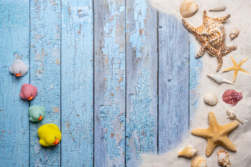 Summer, beach and vacation concept with free text space. Top view. Small group of colorful rubber ducks and sea shell and various sea shells and fine beach sand on an old blue wooden boards background