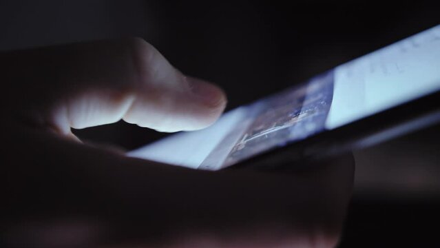 In the Dark: Close-Up of Man Scrolling Screen on Phone with Glare