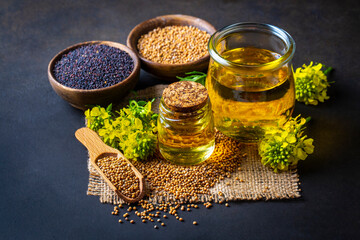 Mustard oil in a glass jar and decanter, mustard grains on a burlap napkin, flowers and leaves on...
