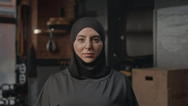 Portrait of young Muslim woman in black hijab posing for camera at boxing club