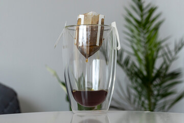 The process of brewing a morning coffee drip with a filter bag in a double-bottomed clear cup