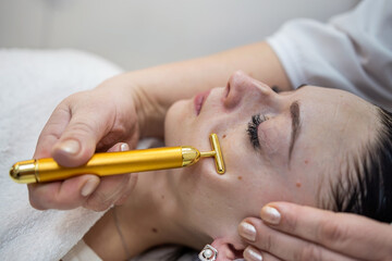 woman receive pulse face massaging at spa, vibrating golden facial massager on female face