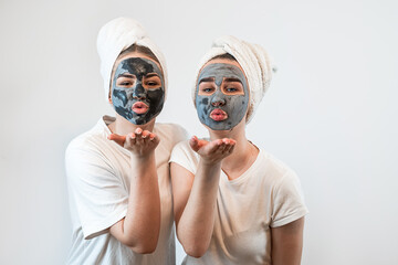 Two younf friends or sisters applying clay facial mask isolated on white