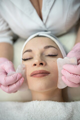 Fototapeta na wymiar cosmetologist masseur doing faacial anti-agging procedure with gouache scraper for her client