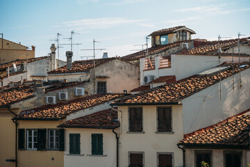 Fototapeta na wymiar The tiled roofs of old houses are illuminated by sunlight on a warm summer day in Italy. The concept of ancient buildings and city attractions