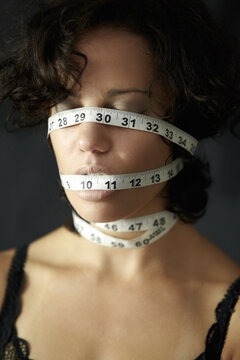 Mental health. a depressed young woman with tape around face and closed eyes. Depression, a person in a black or dark background and insecure about her body with measurements covering her head.