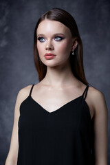 Fototapeta premium Portrait of female in black dress with straps. Woman with earrings in the ear on gray background.