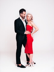 Beautiful fashion woman and her handsome boyfriend in black elegant suit. Sexy blond model in red evening dress. Fashionable couple posing in studio. Brutal man and his female. Isolated on white