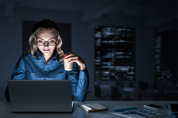 Attractive blonde working on laptop in dark office. Mixed media