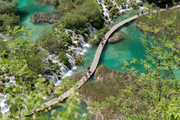 People walking a wooden path through turquoise water in Plitvice national park - Croatia