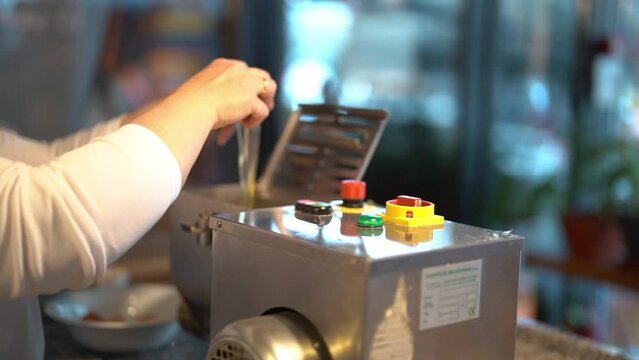 Unanimous female chef breaking two eggs one against each other and adding them into special dough making machine during pasta making process