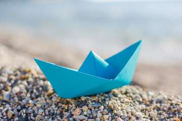 Fototapeta na wymiar Blue paper boat on the pebble beach