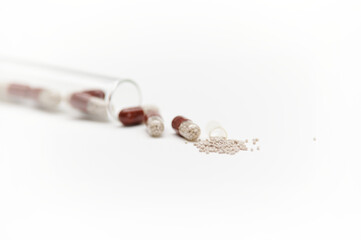 Selective focus: enteric capsules spilling out from gel translucent capsule scattered on white...