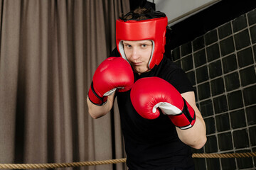 Portrait of a tough guy wearing red head guard helmet and gloves, posing in the ring, looking at...