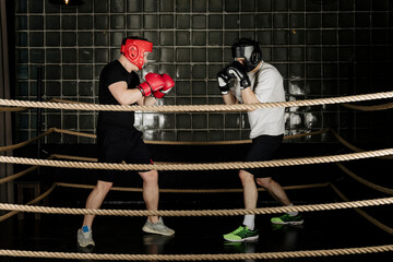 Two big guys boxing and sparring in the ring in head guard helmets and gloves.