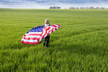Independence Day. National symbol of freedom and independence of the United States of America. child holds American flag behind back and runs through green meadow. Pride to be an American