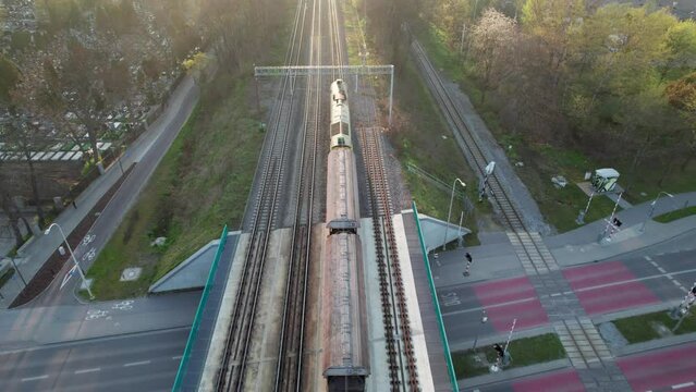A drone-shot captures a freight train passing through the city in the morning, crossing a viaduct and green landscapes. The locomotive pulls empty wagons to be filled with raw materials.