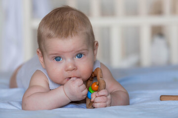 A charming boy in a bright bedroom. A newborn baby is lying on the bed and gnawing on toys. Teeth are teething. The baby's gums are itching. Family, pregnancy and childbirth.