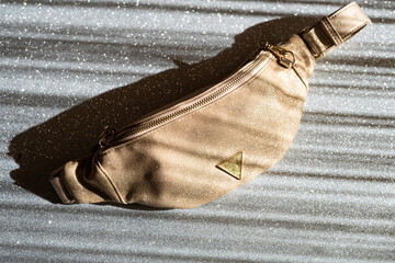 Glamorous women's waist bag in gold color on a gray shiny background. Fashionable handbag with gold chain.