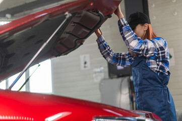 Woman auto mechanic opens the hood of a car in a car service. 