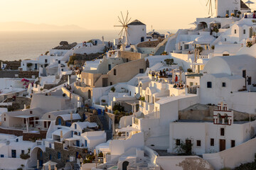 Whitewashed houses and windmills in Oia in warm rays of sunset on Santorini island. Greece - obrazy, fototapety, plakaty