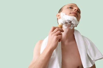 Young man shaving against green background