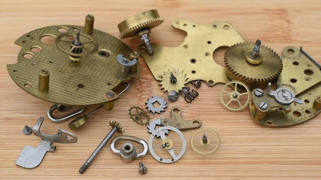 Still life with a gear wheel turning near other elements of clock mechanism on the wooden desk