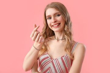 Young woman making heart with her fingers on pink background