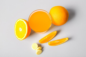 Glass of vitamin C effervescent tablet dissolved in water and oranges on grey background