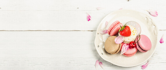Macarons with strawberries, cherries and peonies flower petals, on a white wooden background