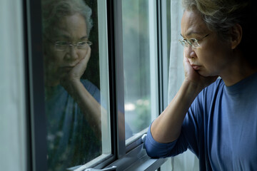Portrait of sad and worried Asian senior woman looking through the window at home - 596594886