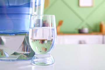 Modern filter jug and glass of water on table in kitchen