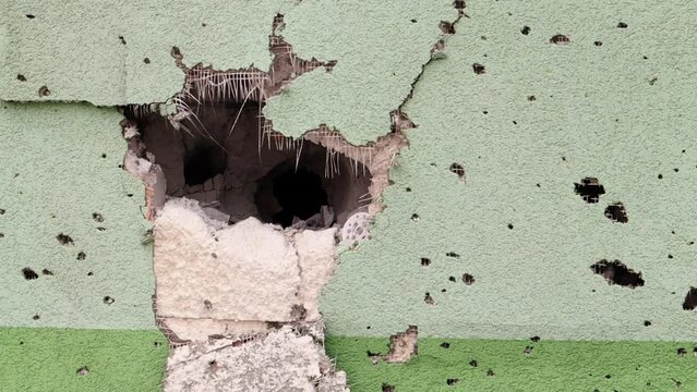 Holes from bullets and shrapnel in the wall on the front line. Scars of war. Concrete wall of a residential building with potholes and holes from gunfire. Consequences of the war in Ukraine.