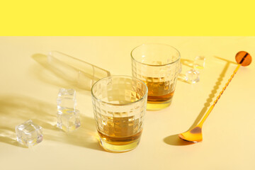 Glasses of rum, ice cubes and spoon on colorful background