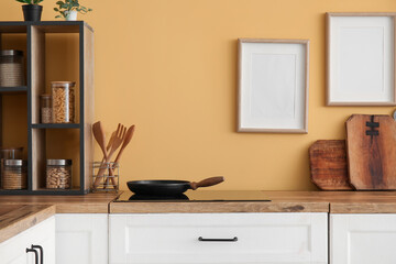 Fototapeta na wymiar Counters with frying pan, stove and kitchen utensils near yellow wall