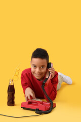 Little African-American boy talking by telephone on yellow background
