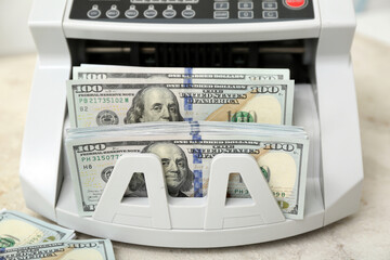 Modern cash counting machine with dollar banknotes on table in room, closeup